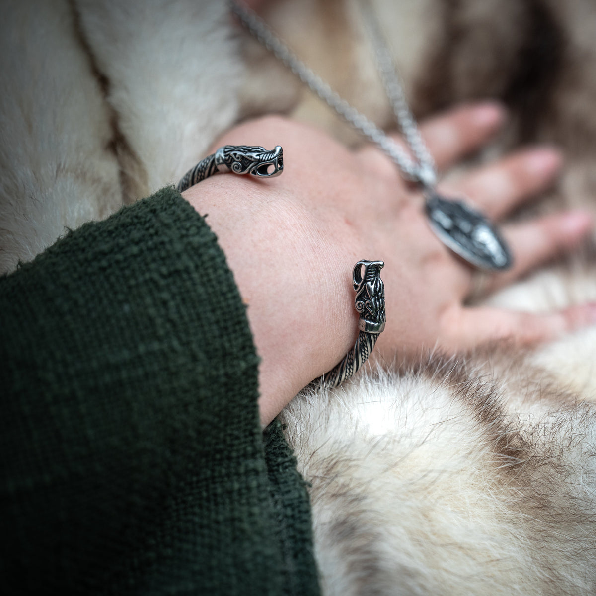 Close-up of the Fenrir Viking bracelet featuring detailed wolf heads, worn on a wrist with traditional Norse-inspired clothing. Ravenritual
