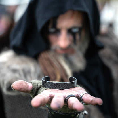 A Viking warrior holding the Norse Heritage Bracelet with engraved Nordic patterns, featuring Viking jewelry by Ravenritual.
