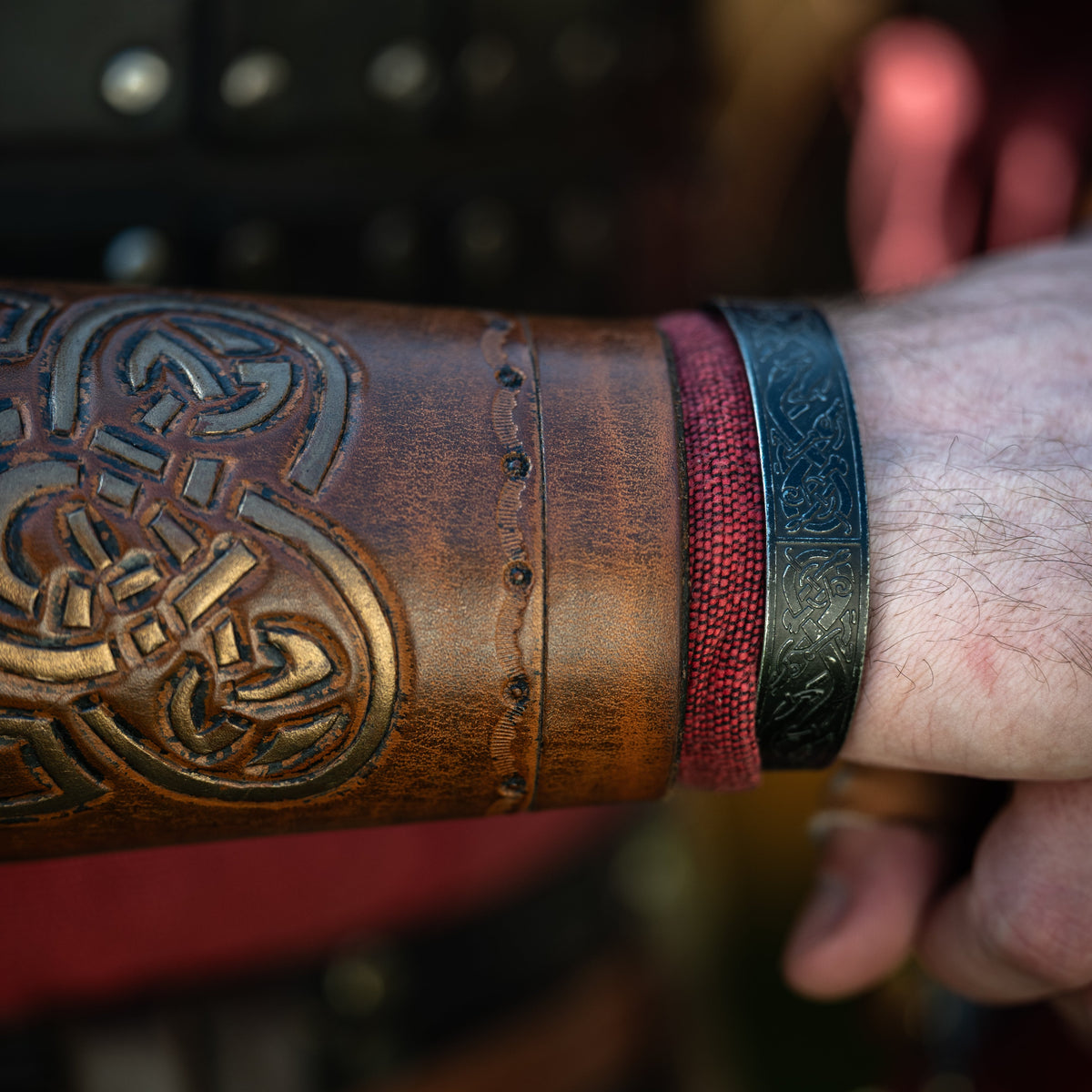 Close-up of the Norse Heritage Bracelet with engraved Celtic knot patterns, worn on a wrist beside a Viking leather bracer.
