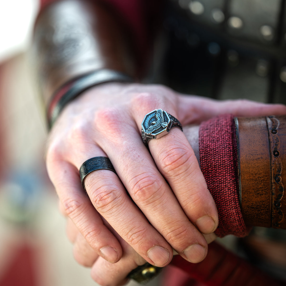 Raven Ring worn on a hand resting against red-brown leather, showing the engraved silver-tone ring in a Viking-inspired setting.