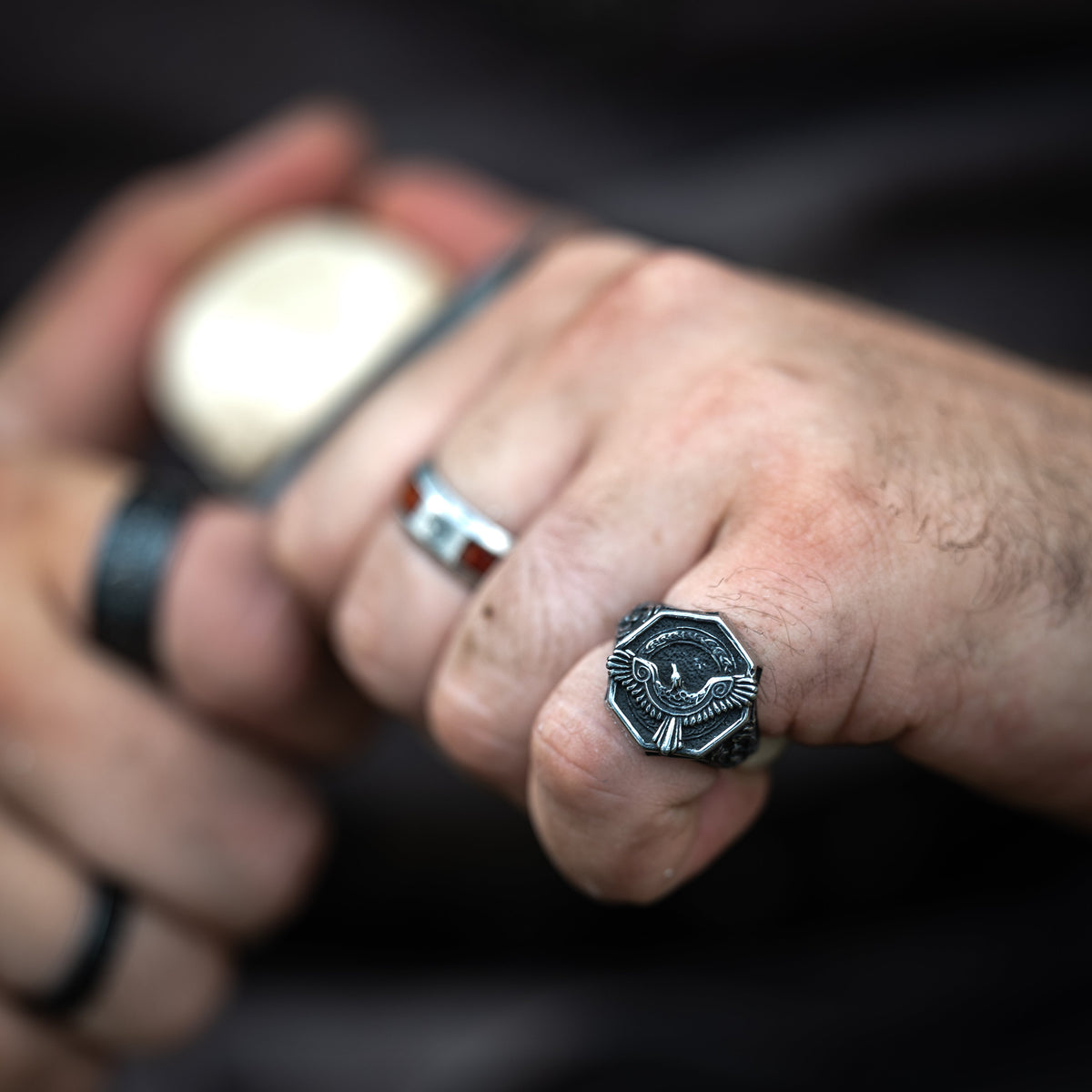 Close-up of a silver-tone Raven Ring worn on a hand gripping a handle, alongside another Viking-style ring.