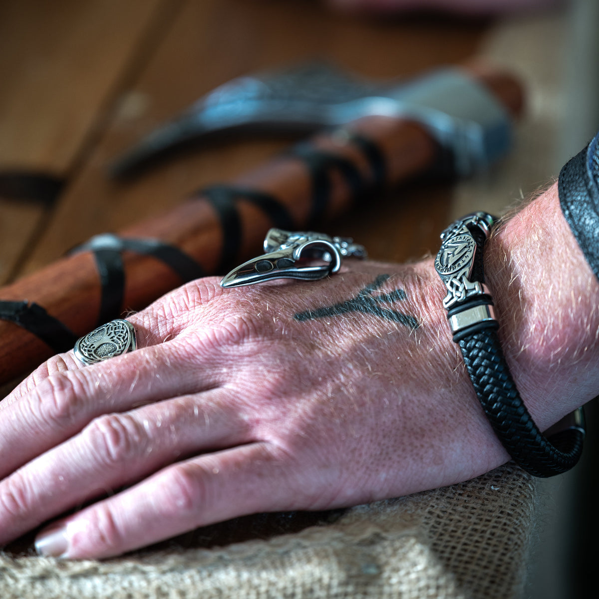 Close-up of the Valknut Bracelet with braided black cord and silver-tone Norse detailing, worn on a wrist beside Viking rings.